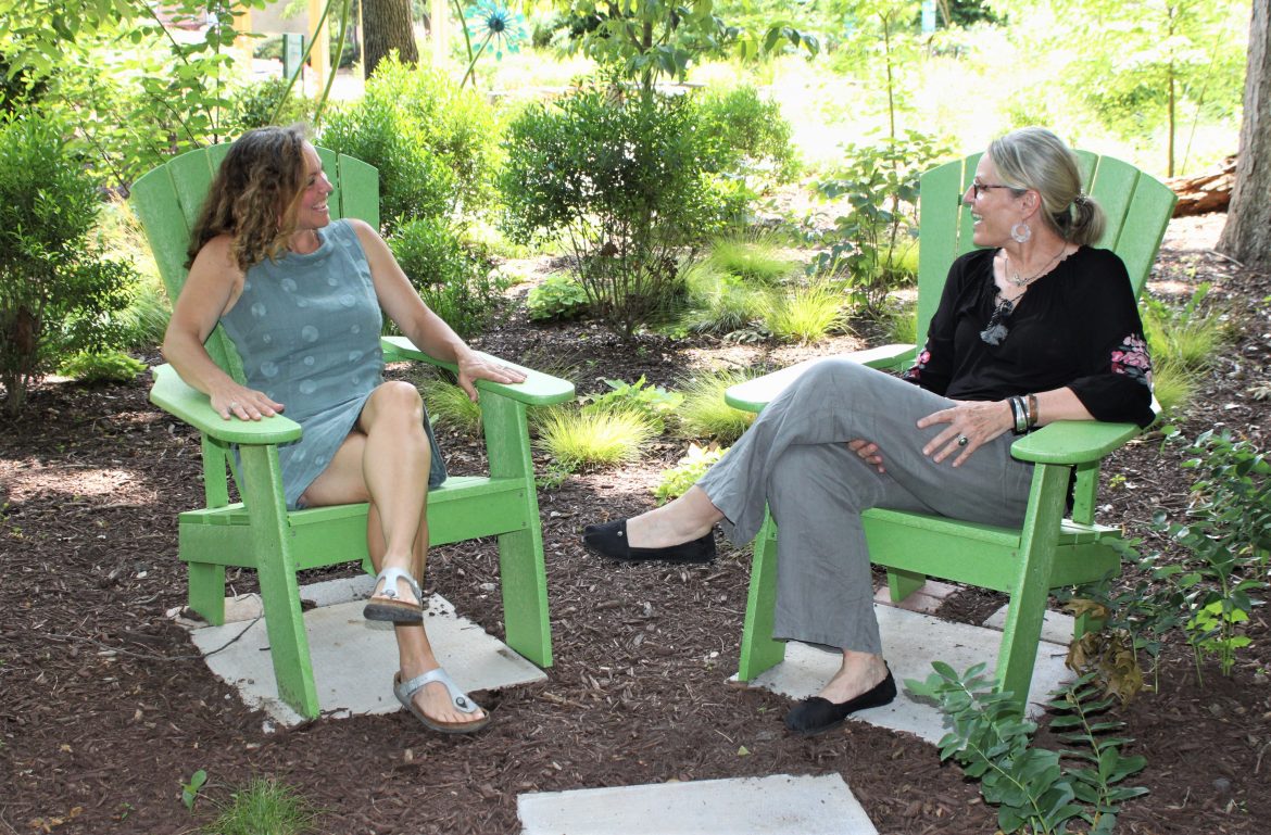 Hospice of the Chesapeake Integrative Arts Volunteers Jill Madey, left, and Teri Jacobson, share a laugh and a smile with each other, as they so often do as friends and partners. They are pictured in a shady spot in the Children's Memorial Garden.