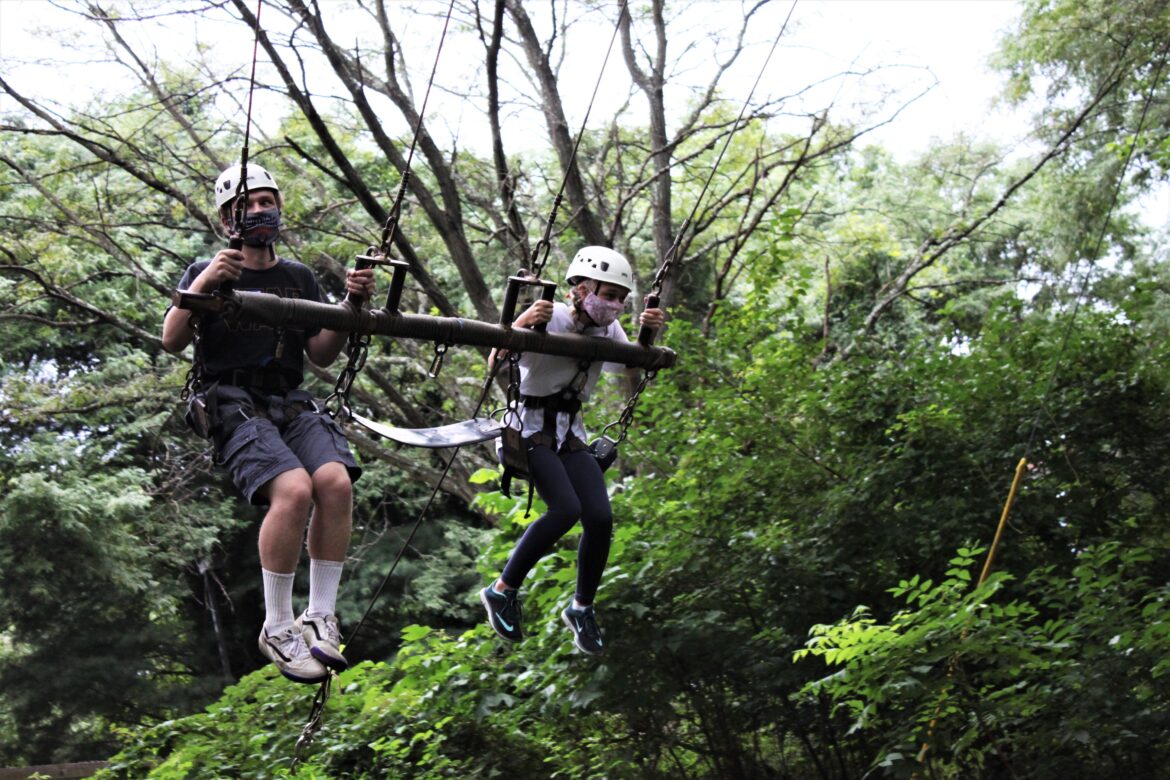 From left, Jeremiah Faust and Lillian Cross ride in a swing that flies high into the tree canopy during Camp Phoenix Teen Grief Camp held at Terrapin Adventures in Savage, Maryland.