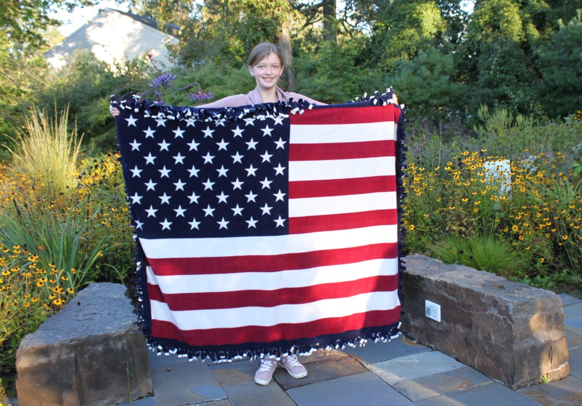 Averie Mortimer holds up one of the no-sew patriotic blankets she created and then donated to our We Honor Veterans program.