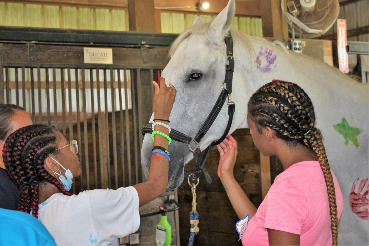 Two teens paint a friendly therapeutic horse at a Chesapeake Life Center workshop held at Maryland Therapeutic Riding in 2022. Photo courtesy of Hospice of the Chesapeake.