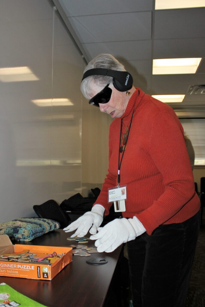 During a Dementia Live training session, a Hospice of the Chesapeake volunteer attempts to assemble a puzzle while wearing dark goggles, oversized gloves and headphones filled with noises. 